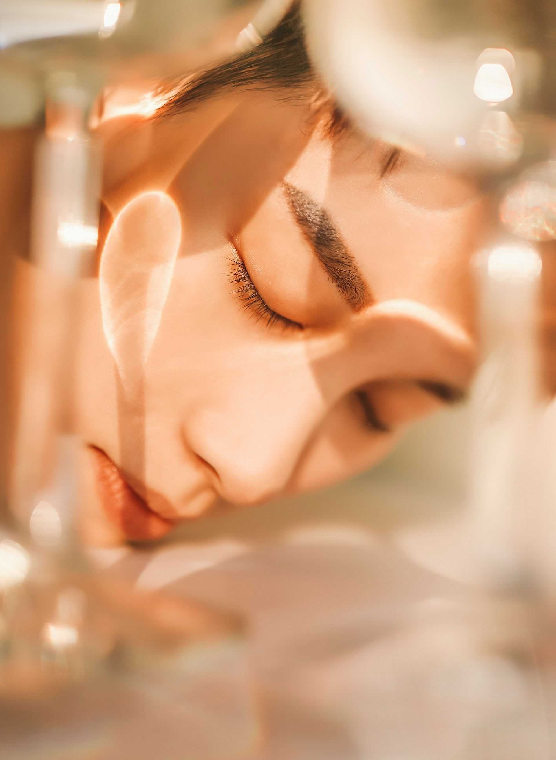A person rests with closed eyes, surrounded by soft, warm light and glass reflections.