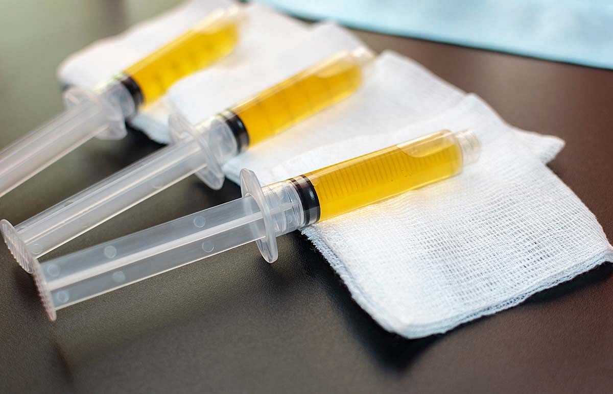 Three syringes filled with yellow liquid placed on white gauze pads on a black surface.